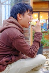 asian teenager boy sitting and chilling eating some bread