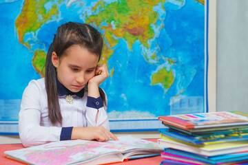 Portrait of a smart cute girl reading books on the background of the world map.