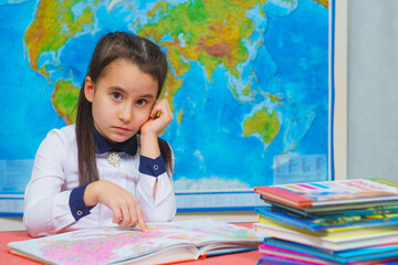 Portrait of a smart cute girl reading books on the background of the world map.