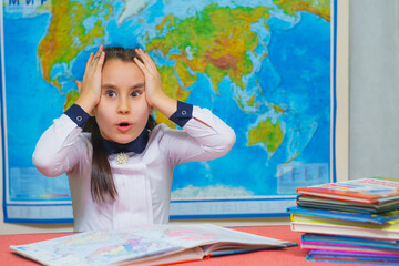 Portrait of a smart cute girl holding her head against the background of the world map.