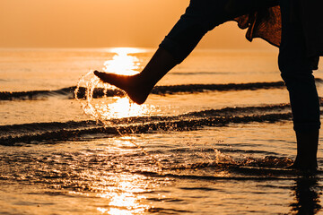 Silhouette of carefree happy female splashing water of ocean with leg during sunset