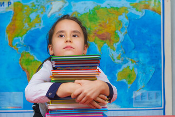 Portrait of a smart cute girl hugging a lot of books on the background of the world map.