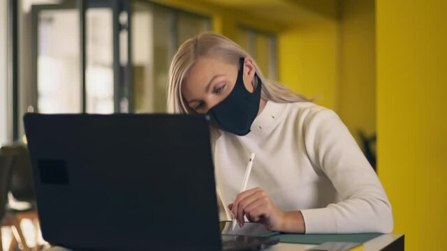 Young Caucasian Girl In Protective Mask Using Laptop And Tablet Online Learning In Web Or Work. Woman Sitting At Table On Office. Work In Pandemic Period. Close Up