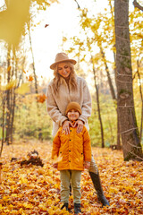 woman with kid boy in yellow and gold autumn forest, mother and son walk outdoor in coats. friendly relationship in family