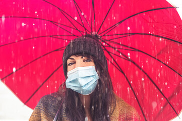 Cheerful pretty girl with face mask protection  holding umbrella while strolling outside in the...