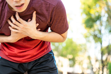 Exhausted male runner athlete suffering painful angina pectoris or asthma breathing problems while running in the park.