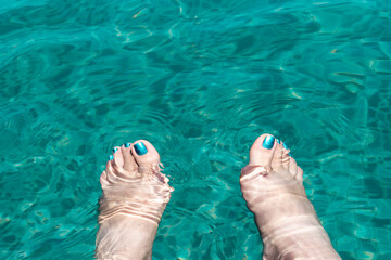Female feet with glitter azure pedicure in turquoise transparent pool water. Concept background...