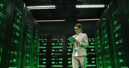 Caucasian beautiful woman walking among servers with tablet device, tapping on screen and checking...