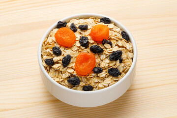 Cup of dry oatmeal with dried fruit on a wooden table.