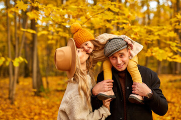 happy family have fun in autumn park nature, caucasian couple and child hugging,kissing, expressing love to each other. in coats outdoors