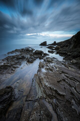 Amazing long exposure seascape with rocky beach at sunrise in the blue hour