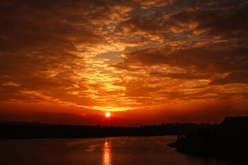 Silhouette of the city and the smoky factories and lake on background of dramatic sky at sunset bright sun and clouds
