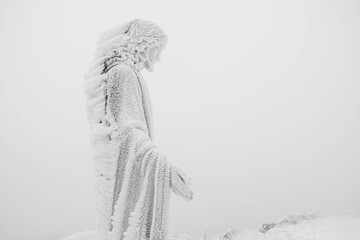 The statue of Jesus is covered with snow and ice on top of the mountain. Copy, empty space for text