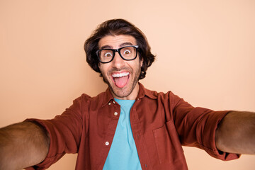 Photo portrait of happy man taking selfie showing tongue isolated on pastel beige colored background