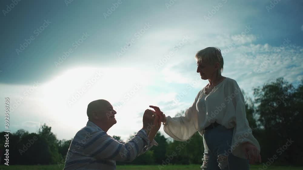 Wall mural senior man making proposal to woman on date in park at sunny day outdoor