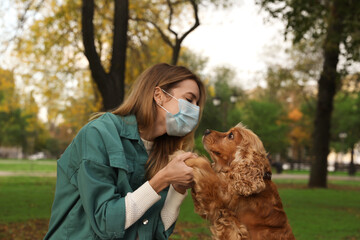 Woman in protective mask with English Cocker Spaniel in park. Walking dog during COVID-19 pandemic