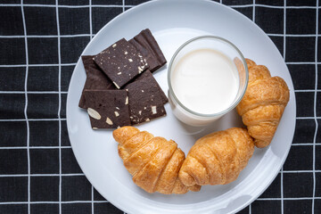 Delicious fresh croissants,cookie and soy  milk in white Plate on black Plaid pattern background. French breakfast. Tasty croissants with copy space
