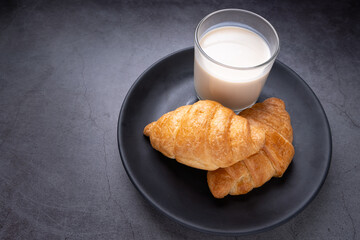 Delicious fresh croissants with soy  milk in black Plate on dark background. French breakfast. Tasty croissants with copy space