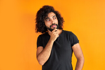 determined arabic male with beard is thinking and looking worried, standing against orange...