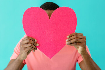 Close up portrait of a young man holding pink heart in front of head with face obscured, valentineÕs day love, give your heart concept