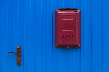 Modern red mailbox on a blue iron fence, wall with door
