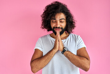 Fototapeta na wymiar young man keeps hands together, pray, being cordial and friendly, expresses gratitude at camera isolated over pink background
