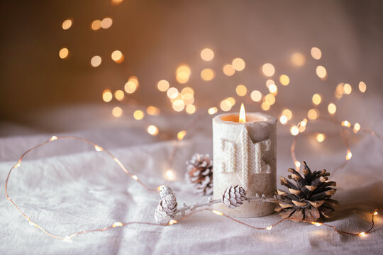 Natural Christmas decoration with burning candle on white linen and pine cones  -  magic lights in background