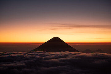 Fototapeta na wymiar The volcano peaks its head out above the clouds at sunrise.