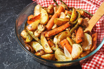Baked vegetables on black stone background. Potatoes, carrot, mushrooms and onions