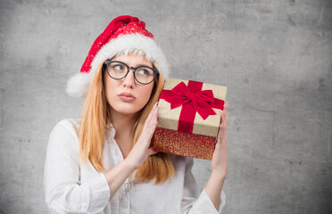 Thoughtful Santa woman with christmas gift isolated on gray background. Young girl wearing red santa hat and holding present box. Studio shot
