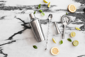 Cocktail set on the marble background - lemons, limes, shaker, spoon, ice