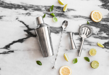 Cocktail set on the marble background - lemons, limes, shaker, spoon, ice