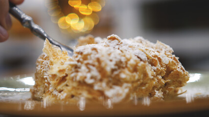 Tasty dessert. Slice of Napoleon cream cake, made from puff pastry, lies on a plate on a table in a restaurant