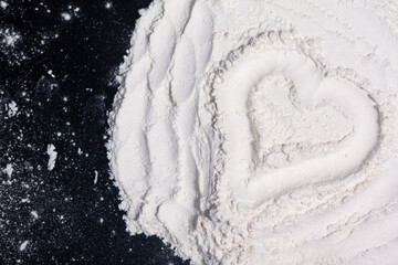 A pile of flour on a dark surface. Drawing of a heart.