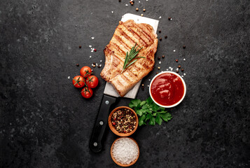 grilled pork steak with spices over a meat knife on a stone background