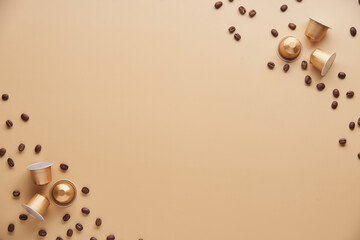 Caffeine, hot drinks and objects concept - close up of golden capsules or pods for coffee mashine with some roasted grains on beige background. Top view with space for text. Flat lay..