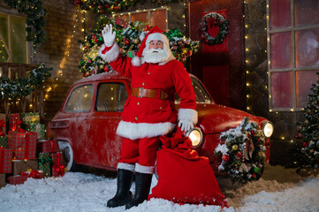 Santa Claus poses near a red classic car. Merry Christmas