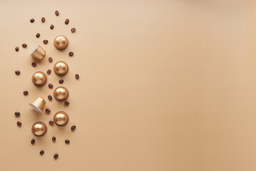 Caffeine, hot drinks and objects concept - close up of golden capsules or pods for coffee mashine with some roasted grains on beige background. Top view with space for text. Flat lay..