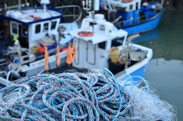 The harbor of the seaside town Whitstable in Kent, UK, closeup of fishing nets, blurred colorful fishing boats in the background - obrazy, fototapety, plakaty