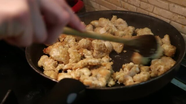 Preparing delicious crispy sweet and sour asian chicken nuggets on a teflon frying pan, using olive oil, close-up