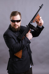 Mature man in sunglasses dressed in suit with tommy gun