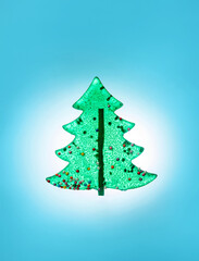 A lollipop shaped like a Christmas tree is placed in front of a shining background in pastel blue.