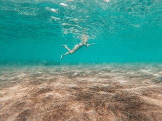 Obraz premium Underwater view in blue sea ocean water of active woman swimming and enjoying the summer holiday vacation at the beach