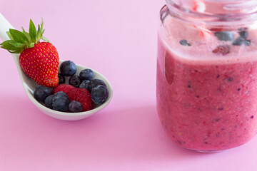 Pink strawberry smoothie with fresh fruits (strawberry, blueberries and raspberries)in a spoon on pink background.Healthy natural fruits juice drink concept.