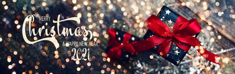 Merry Christmas and Happy New Year 2021 - gift box with golden stars and red bow on wooden...