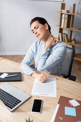 Businesswoman with hurting neck sitting on office chair at workplace