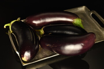 Several ripe dark eggplant, close-up, on a black background.