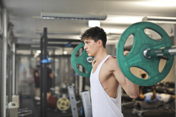 young man trains with barbell in the gym