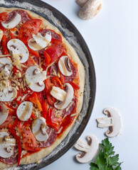 Uncooked pizza with mushrooms, salami, tomatoes, peppers and cheese.