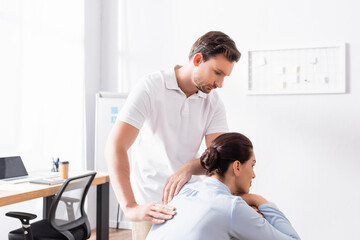 Focused masseur looking at brunette woman, while doing back massage in office